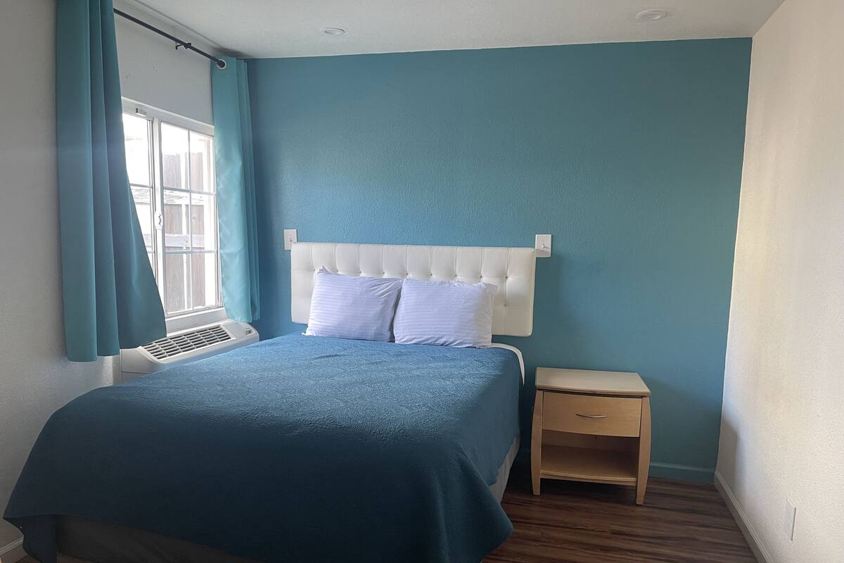 Un dormitorio con cama, mesita de noche, ventana con cortinas y un calentador de pared.