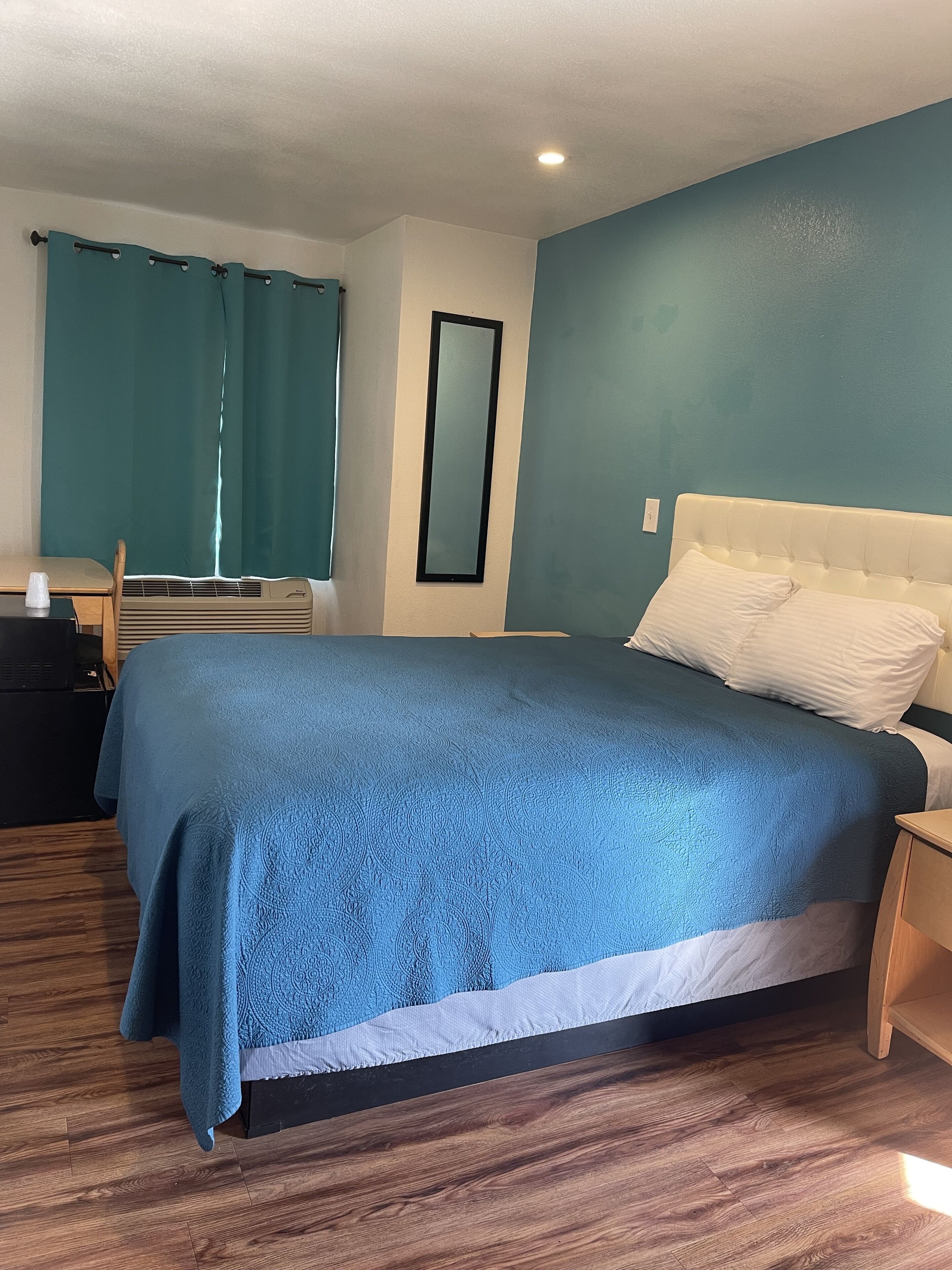 A bedroom with a bed, a nightstand, a chair, a desk, and a mirror.