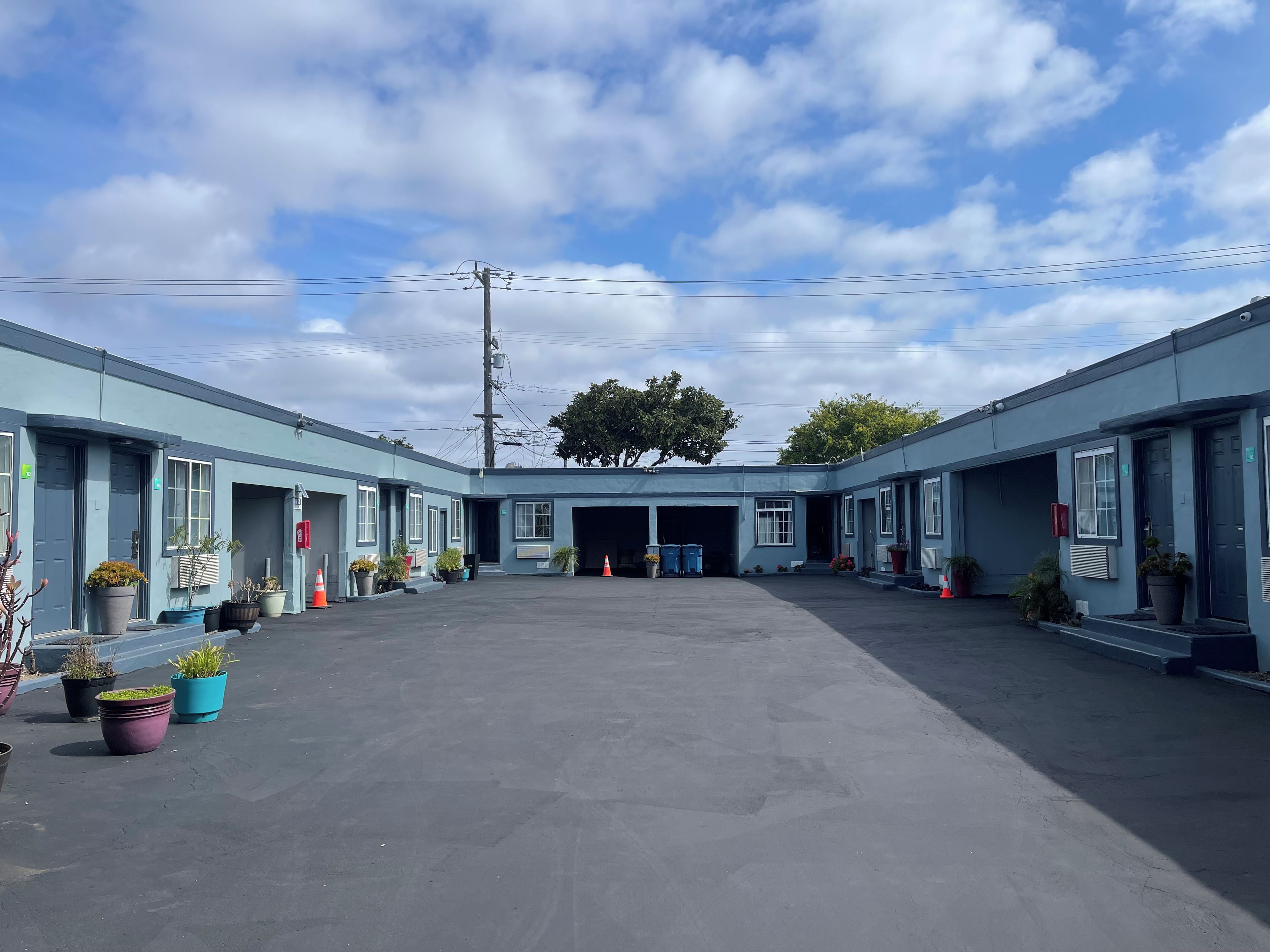 A motel with a central garage, potted plants, and a clear sky.
