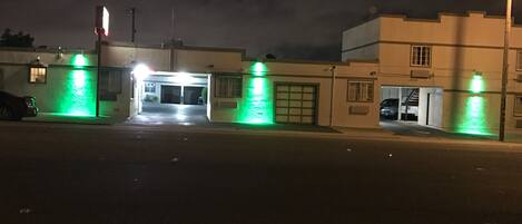 Un área de estacionamiento cerrada con acceso para garaje, un automóvil aparcado a la izquierda y un edificio con puerta de garaje a la derecha.