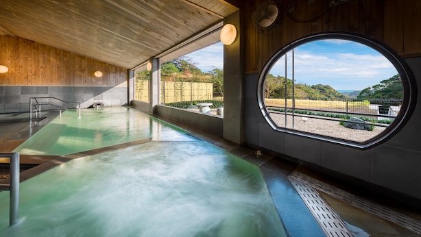 Un spa con hidromasaje, techo de madera y vista a un jardín a través de un amplio ventanal.