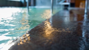 Una piscina interior larga y estrecha, con agua cristalina, suelo liso y barandilla de vidrio.