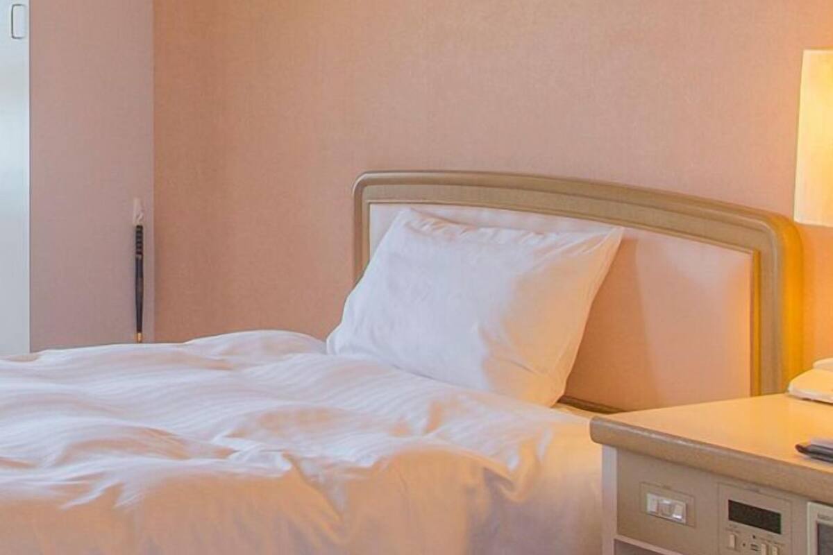 A hotel room with two beds, a nightstand with a lamp, and a wall-mounted control panel.