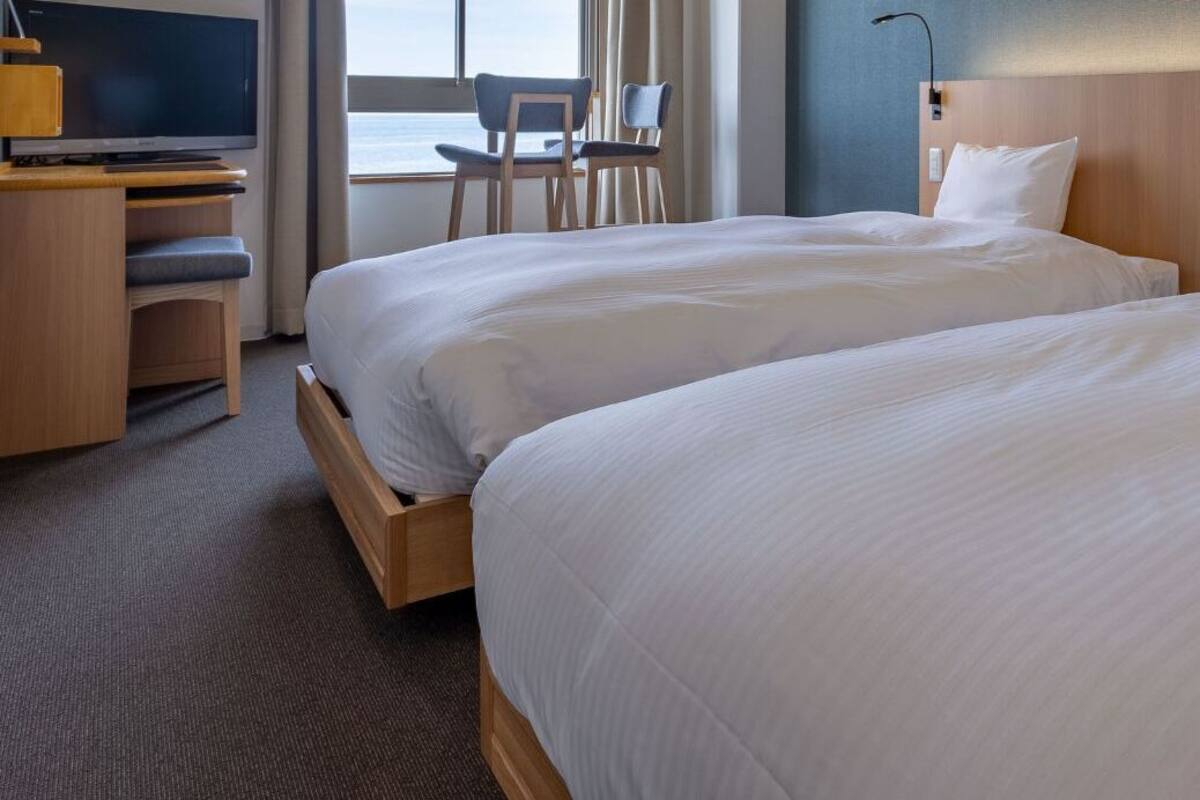 A hotel room with two beds, a desk with a TV, and a view of the sea.