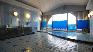 An indoor swimming pool with tiled walls and a tiled floor, large windows with blue ocean-themed designs, and a ceiling with a grid pattern.