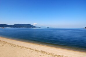 Una playa con aguas azules cristalinas, orilla de arena y colinas a lo lejos.
