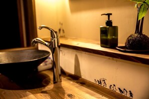 A bathroom with a wooden vanity, a black basin, a modern faucet, and a green soap dispenser. - Dot Hostel Nagano (Nagano)