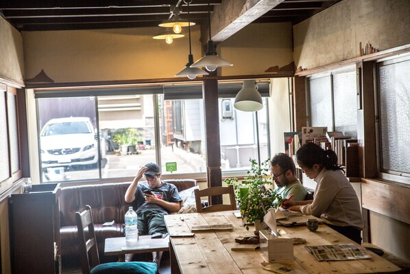 A cafe with wooden tables and benches, large windows, and hanging pendant lights. - Dot Hostel Nagano (Nagano)