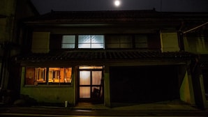 Una casa tradicional japonesa de noche, con una luna visible en el cielo.