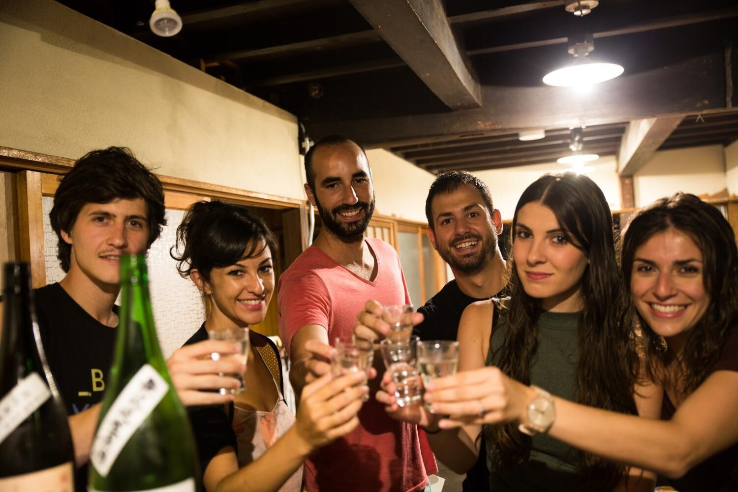 Un grupo de personas brindando con vasos a una mesa con botellas.