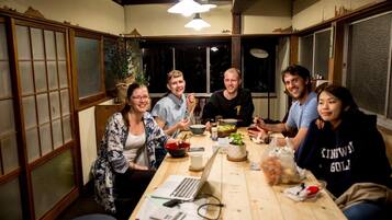 A group of people sitting around a wooden table with food and drinks, in a room with traditional Japanese sliding doors and a ceiling fan.