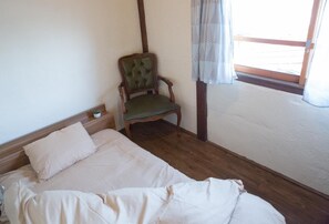 A small, simple room with a bed, a wooden chair, and a window with curtains. - Dot Hostel Nagano (Nagano)