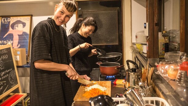 Una cocina con dos personas cocinando, un menú en una pizarra y diversos utensilios de cocina.