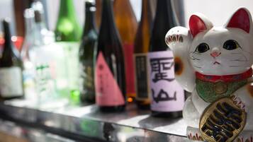Eine Auswahl an Flaschen mit Etiketten, darunter eine mit japanischen Schriftzeichen, sowie eine dekorative Katzenfigur mit Medaille.