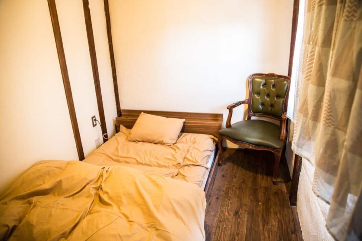 A bedroom with a wooden bed, a green upholstered chair, and a window with curtains.