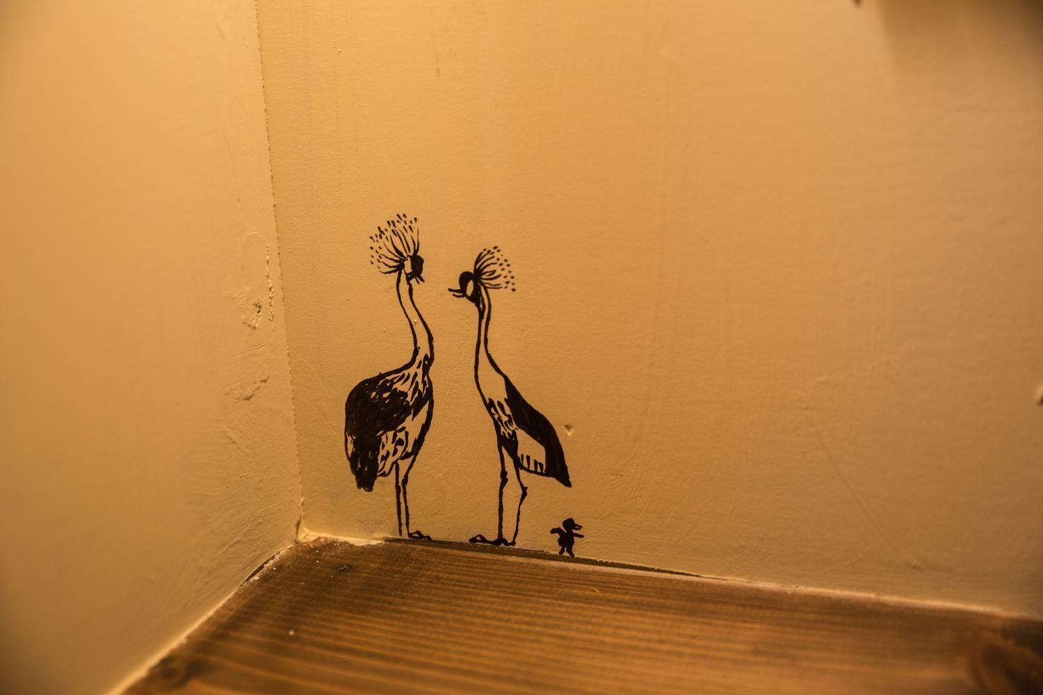 Un mur orné d’une fresque représentant deux oiseaux, l’un plus grand et l’autre plus petit, perchés sur une étagère en bois.
