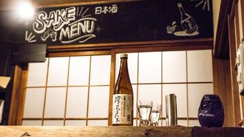 A bottle of sake on a wooden counter with glasses and a metal container, in front of a sign with Japanese characters and a menu.