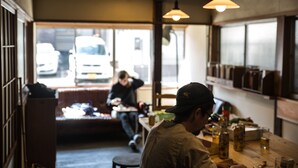 Interior de un restaurante con mostrador de madera, lámparas colgantes y vista a la calle.