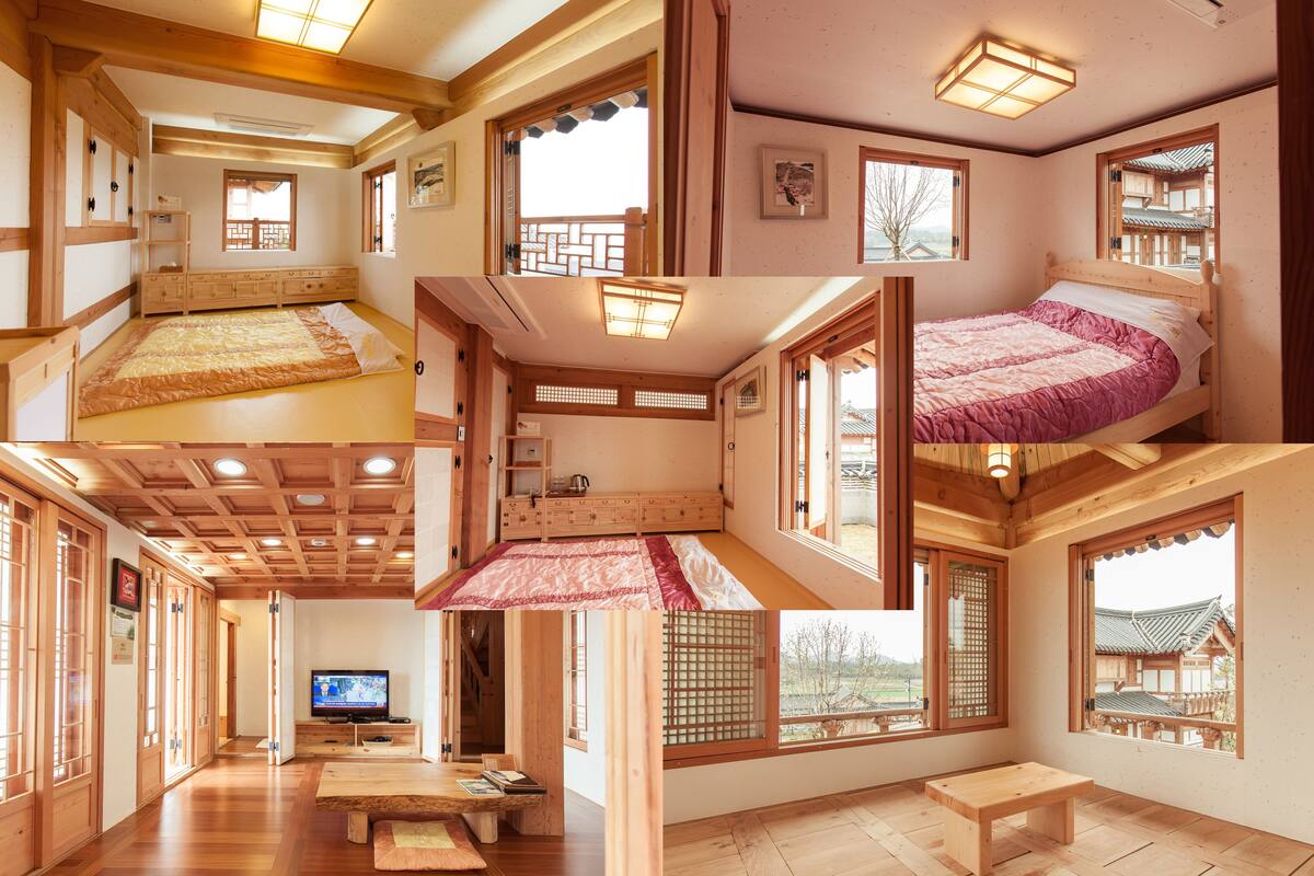 A traditional Japanese-style room with tatami flooring, a low wooden bed, a television, and a view of a traditional building outside.
