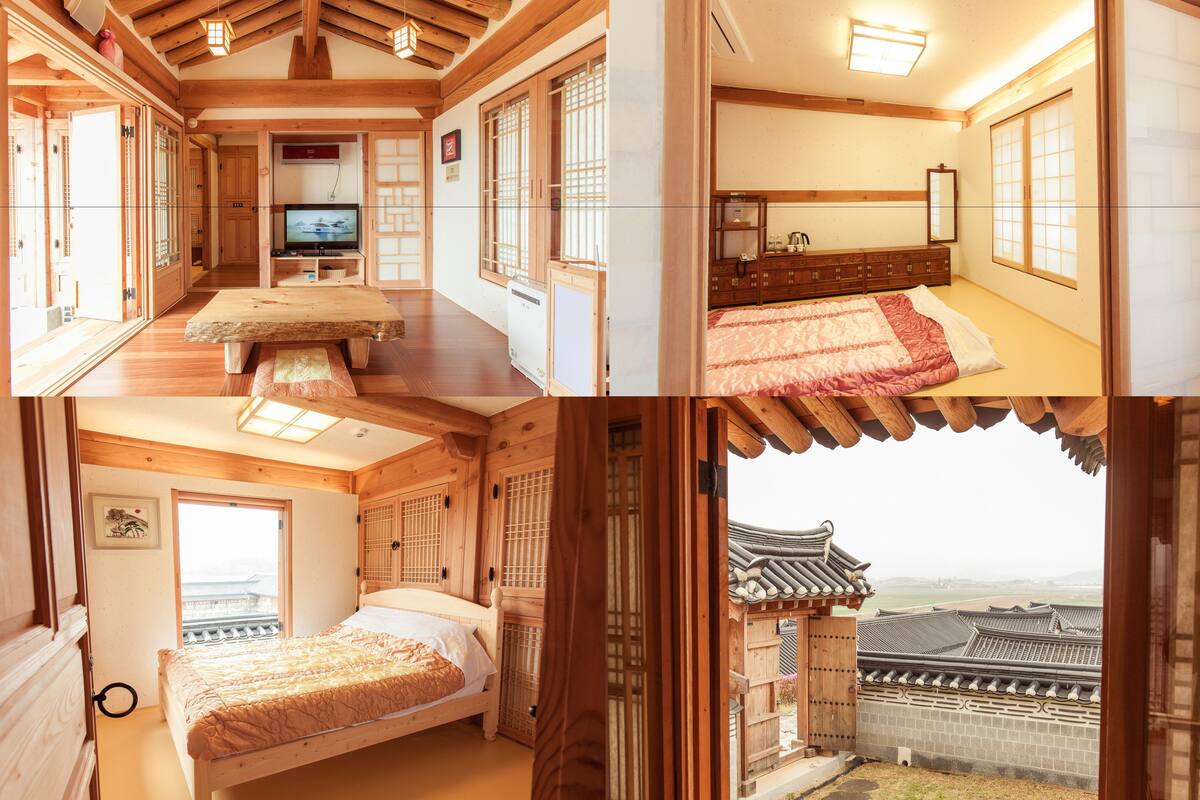 A traditional Japanese-style room with tatami flooring, a bed with a red and white bedding, a television, and a view of a traditional Korean palace through a wooden door.