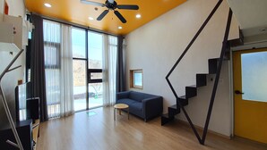 Una sala de estar moderna con suelo de madera, un sofá azul, un ventilador de techo y una escalera de diseño único.