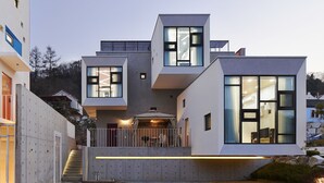 Una casa moderna de varios pisos con amplios ventanales, un balcón y una escalera que conduce a los niveles superiores.
