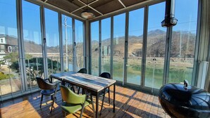 Una habitación soleada con una mesa grande y sillas, una parrilla y vistas a un lago y montañas a través de amplias ventanas.
