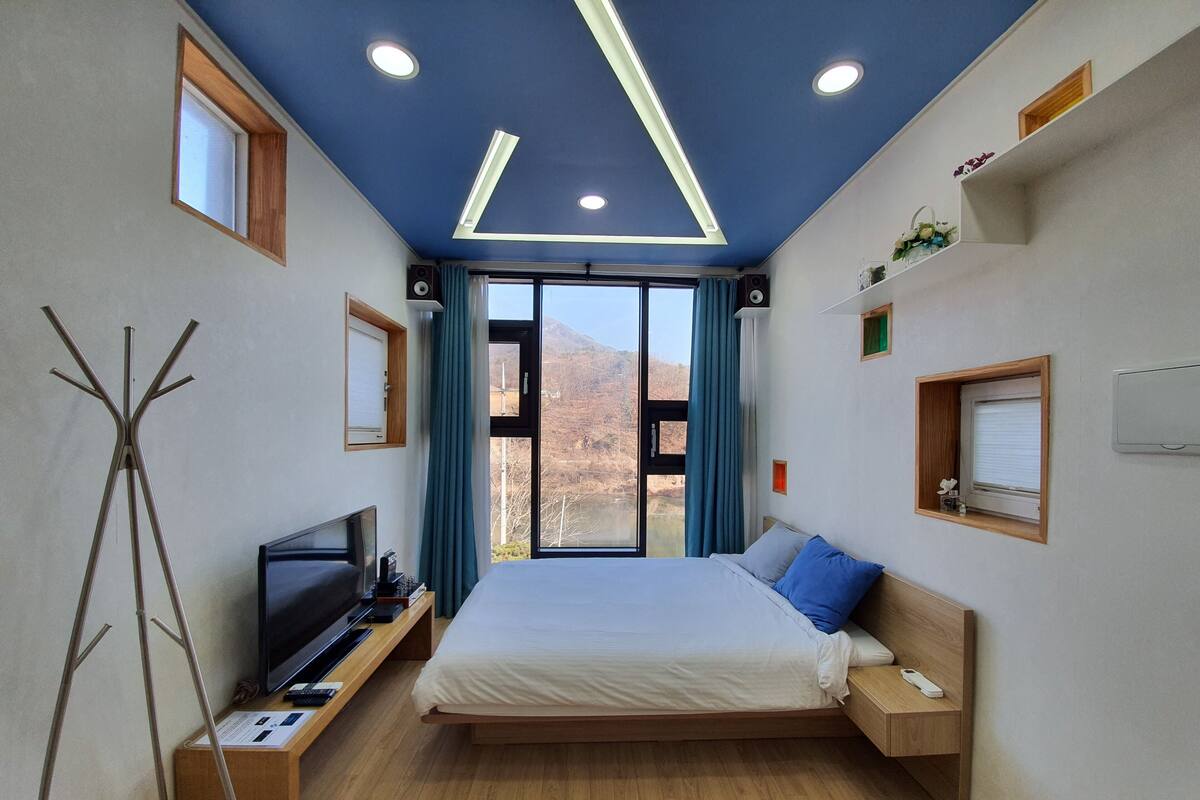 Ein modernes Hotelzimmer mit einem großen Bett, einem Fernseher, Holzboden und Bergblick aus dem Fenster.