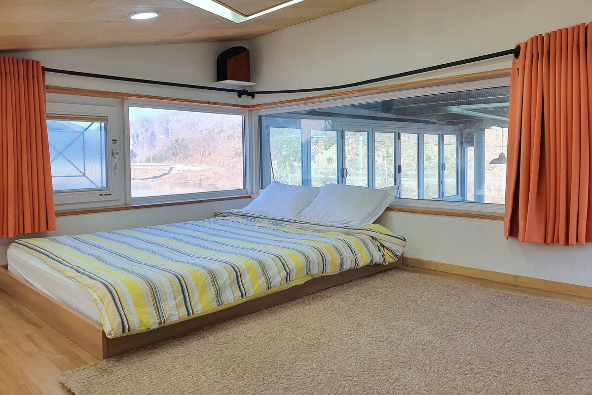 Ein Schlafzimmer mit Bett, großen Fenstern und Blick auf eine Brücke.