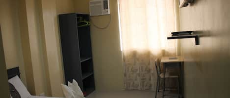 Una habitación de hotel con cama, escritorio, silla, armario y ventana con cortinas.