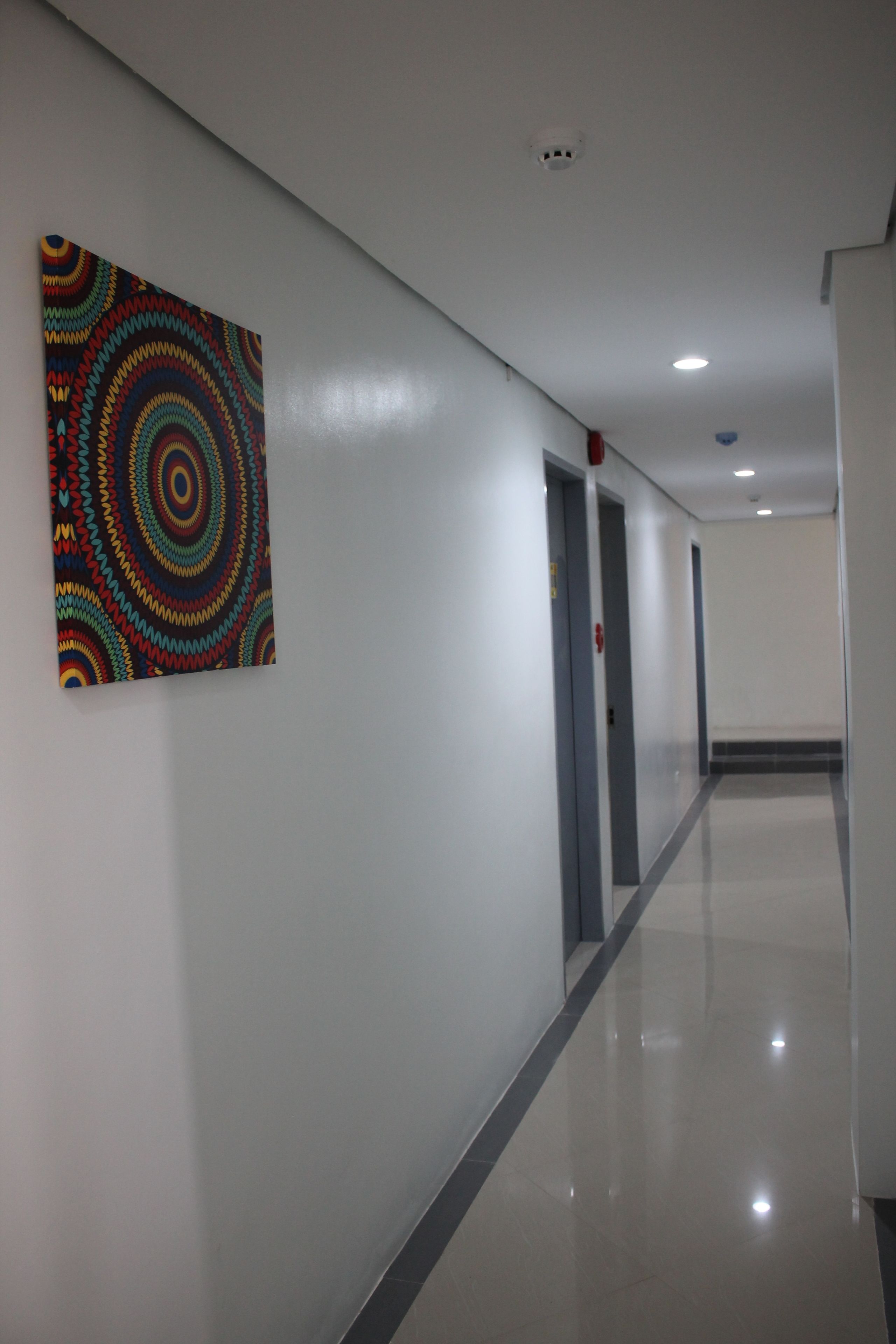 Un couloir orné d’une œuvre d’art colorée au mur, muni d’un détecteur d’incendie et doté d’un sol propre et brillant.