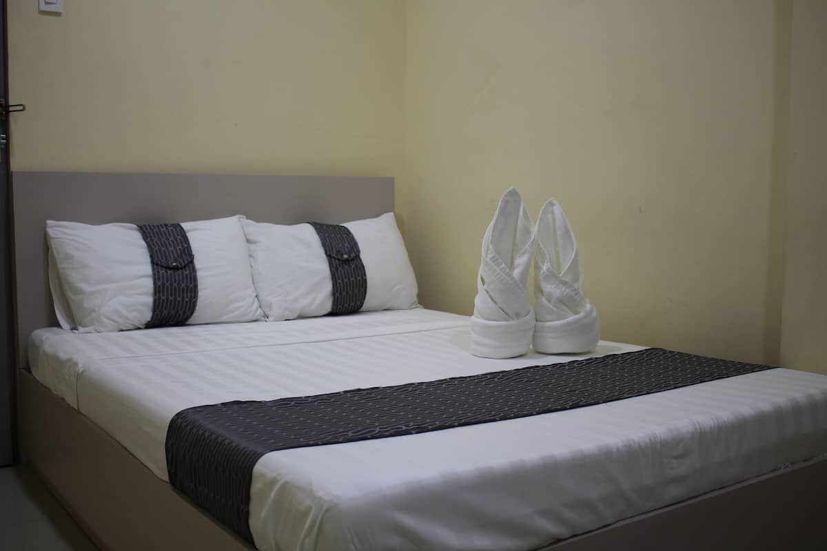 A neatly made bed with white linens, two pillows, and a dark blanket.