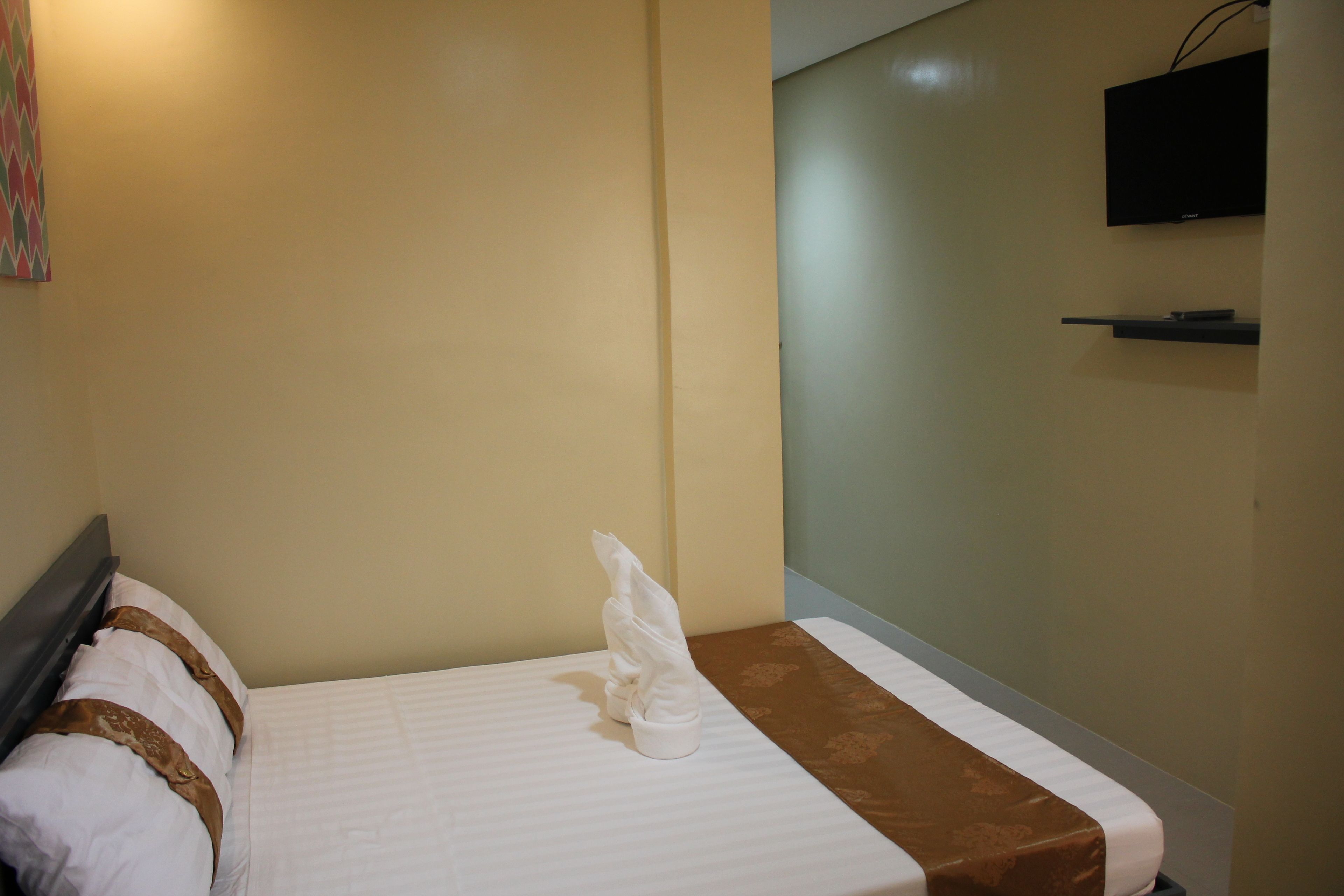 Habitación de hotel con cama, un televisor de pantalla plana montado en la pared y un estante pequeño debajo.