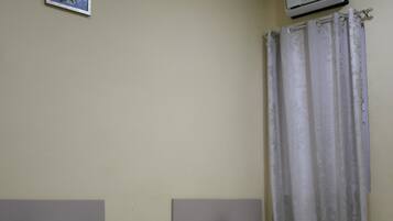 Two single beds with white linens and dark headboards, a small bedside table with a lamp, and a wall-mounted air conditioner.