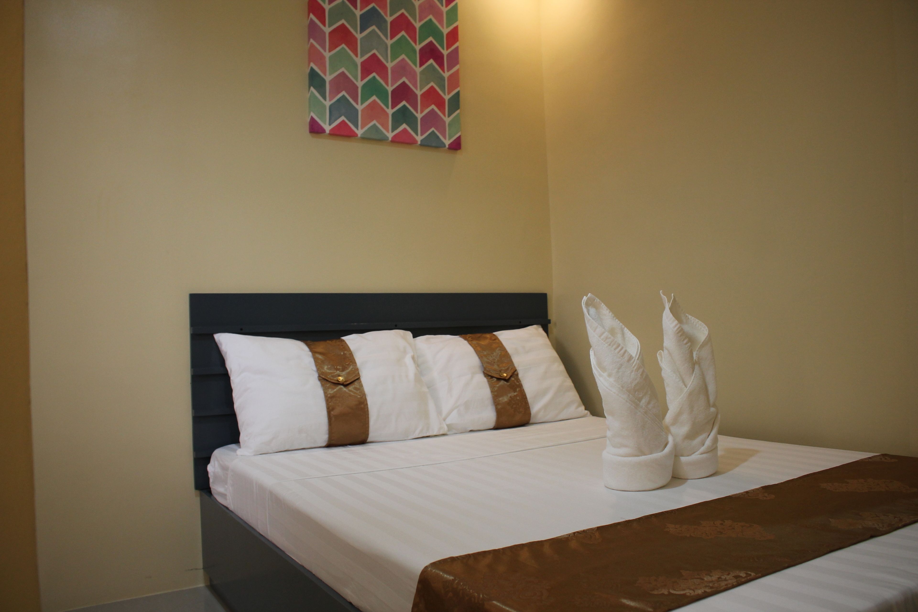 Una cama bien hecha con ropa de cama blanca y almohadillas decorativas marrones, un edredón marrón y una obra de arte colgada en la pared sobre la cama.