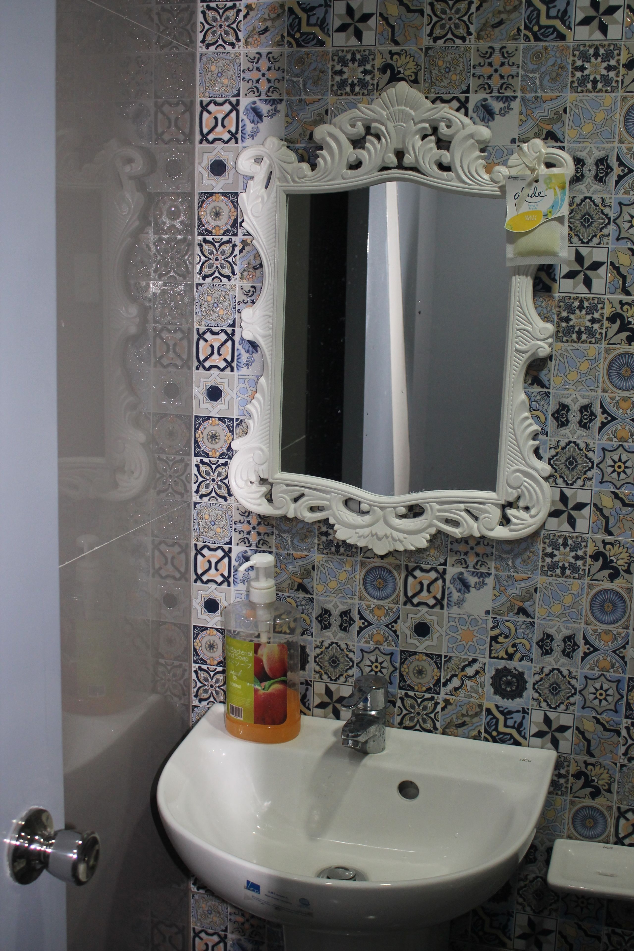 Un baño con lavamanos blanco, espejo decorativo y salpicadero de azulejos ornamentales.