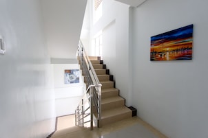 Una escalera moderna con barandilla de metal que conduce a un rellano con un cuadro de una escena de atardecer.