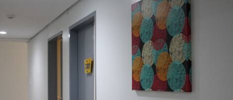 Un pasillo con dos puertas, una con el número 207, y un cuadro abstracto y colorido en la pared.