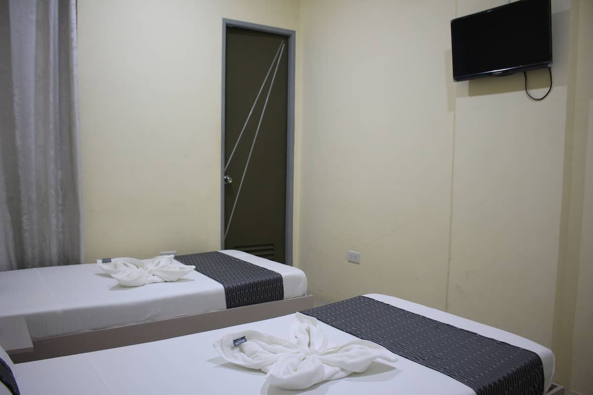 Two single beds with towels, a television on the wall, and a door with a towel rack.