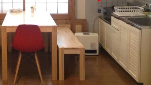 A small dining area with a wooden table and benches, a red chair, and a view through a window. - Condominio Mozu 102 (Sakai)