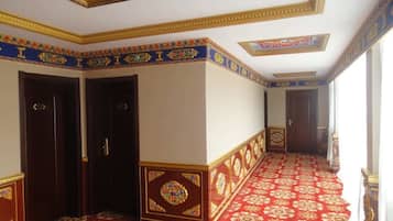 A hallway with red carpet, ornate gold and blue trim, and a patterned ceiling.