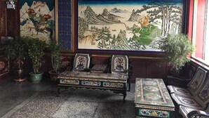 Una habitación tradicional con un mural grande, un banco de madera y una mesa con diseños intrincados.