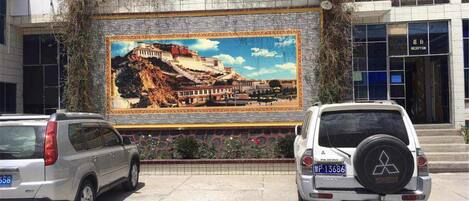 A building with a large mural of a historical site, two parked cars, and a reception sign.