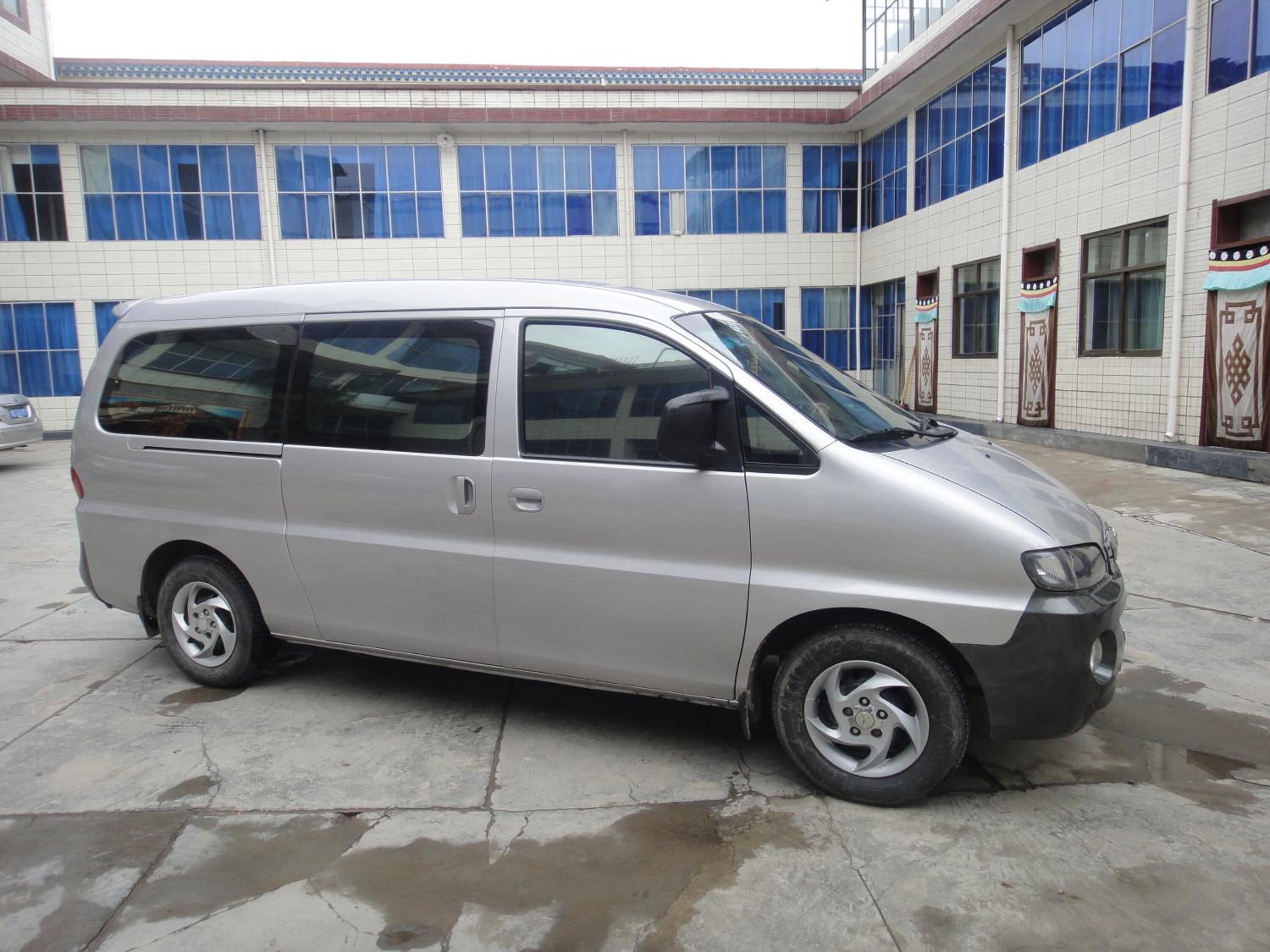 A silver minivan parked in front of a building with large windows and a tiled facade.