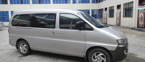A silver minivan parked in front of a building with large windows and a tiled facade.