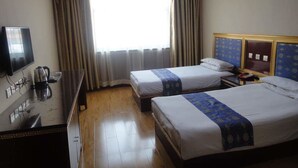Habitación de hotel con dos camas, un escritorio con televisor y una ventana con cortinas.