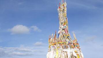 A large, colorful, multi-tiered structure with flags, set against a clear blue sky and surrounded by green hills.