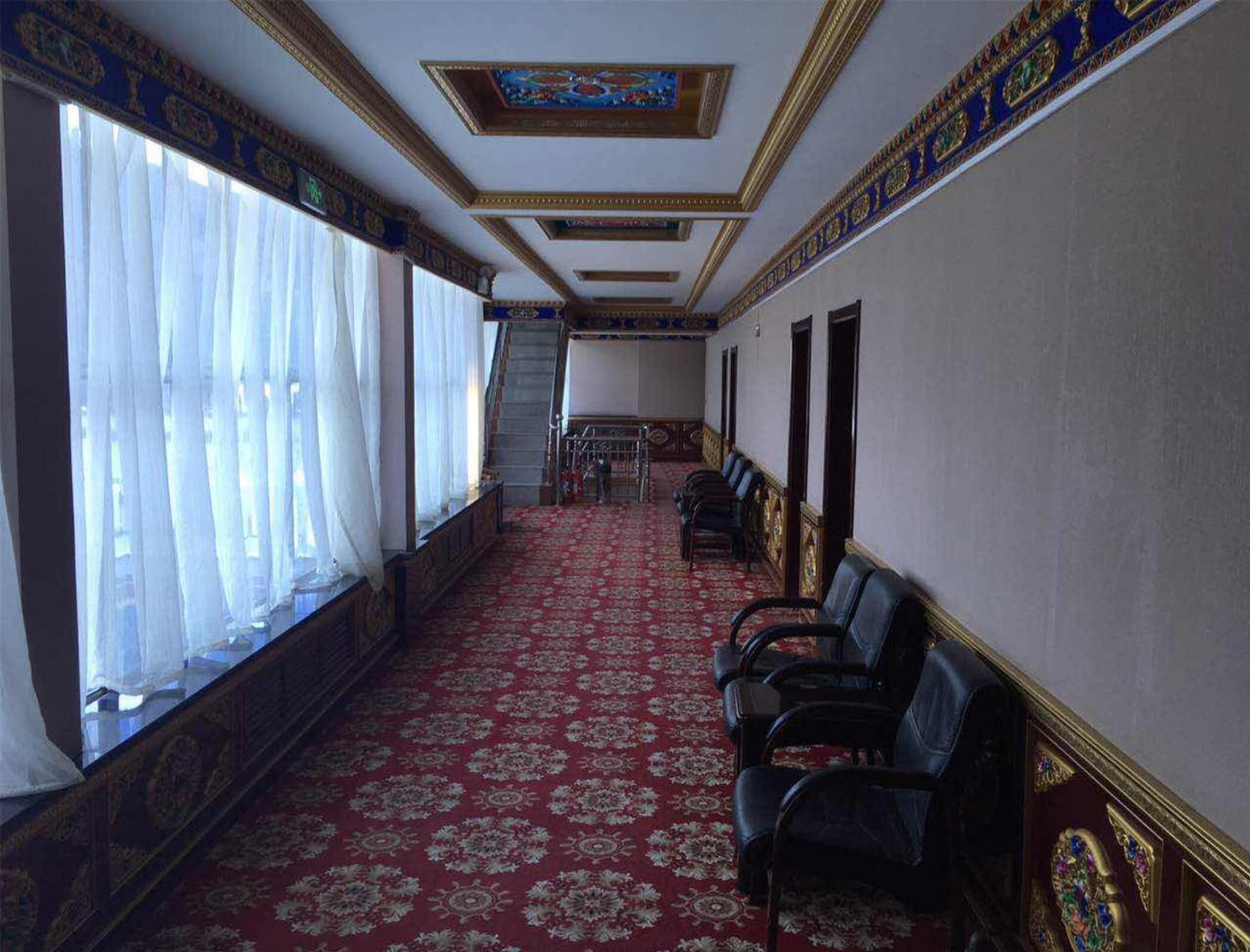 Un couloir avec un tapis rouge, des rangées de fauteuils en cuir noir et un escalier menant à une pièce dont le plafond est blanc.