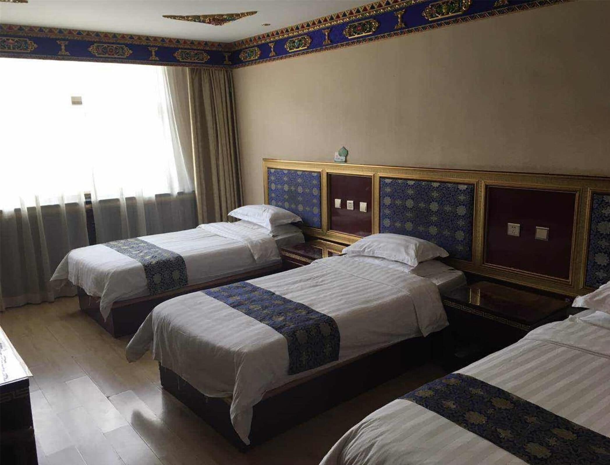 A hotel room with three single beds, a wooden headboard, a small bedside table, and a window with curtains.