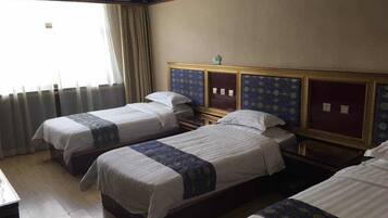 A hotel room with three single beds, a wooden headboard, a small bedside table, and a window with curtains.